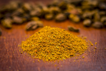 Raw black cardamom with its powder on a brownish wooden surface.