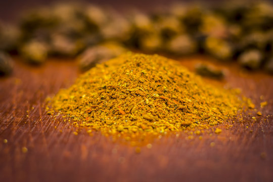 Raw black cardamom with its powder on a brownish wooden surface.