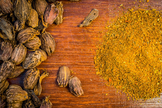 Raw black cardamom with its powder on a brownish wooden surface.