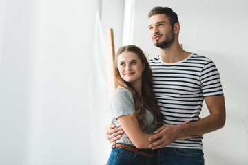 Naklejka premium young couple embracing near window and looking somewhere