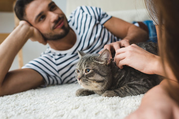 young couple petting cat while lying on floor at home