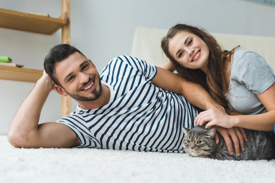 beautiful young couple lying on floor with adorable tabby cat