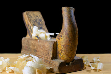 Old plane and shavings on wooden table. Isolated on black, room for text.