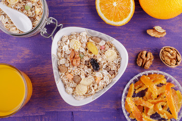 Healthy breakfast. Ceramic bowl with oat flakes, dried fruits, nuts on a violet wooden background