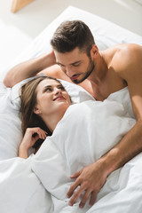 smiling young man embracing girlfriend from behind in bed in morning