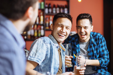 The company of handsome young men having fun together. Friends laughing and drinking beer at the bar
