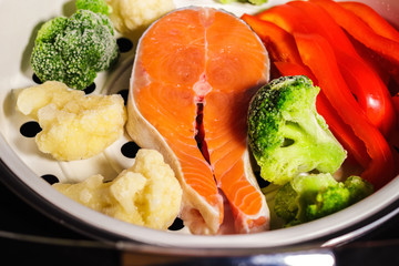 Raw salmon steak, fresh bell pepper, frozen vegetables: broccoli and cauliflower in a multi-cooker tray for steaming