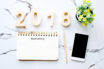 2018 resolution on blank notebook paper and smart phone on white marble background, new year business and technology concept, template