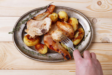 hand with fork against roasted chicken with potatoes