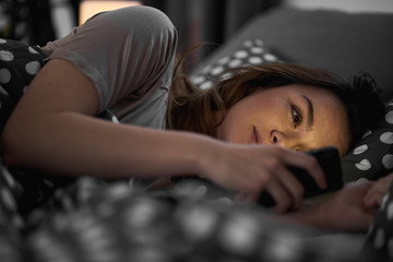 Fototapeta na wymiar Girl using smart phone and lying down in bed late at night