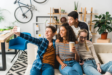 happy multiethnic teenagers sitting on sofa and taking selfie with smartphone