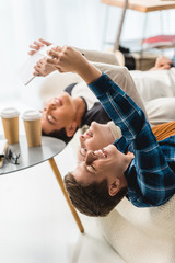 caucasian teenagers lying on sofa and taking selfie with tablet and smartphone