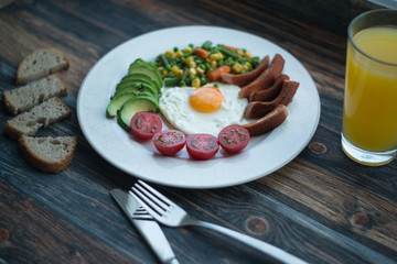 English breakfast. Fried eggs, sausages, avocado, beans, toasts, tomatoes, orange juice on wooden table. Top view with copy spac