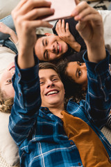 overhead view of multicultural teens taking selfie while lying on bed