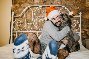 .Funny Christmas image of a handsome young boy playing with his brown spanish water dog on top of his bed. Lifestyle.