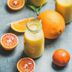 Obraz na płótnie Canvas Healthy yellow smoothie with citrus fruit and ginger in bottle over grey concrete background, selective focus, square crop. Clean eating, dieting, weight loss, vegetarian, vegan food concept