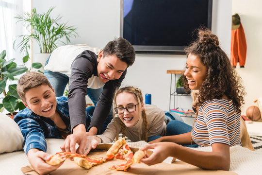 happy multicultural teenagers taking pizza
