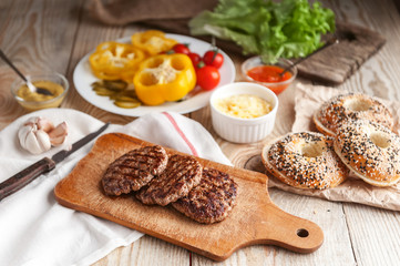 Ingredients for a delicious home burger on a wooden background. roll, bagel, with a juicy cutlet from beef, sauces cheese fresh lettuce leaves