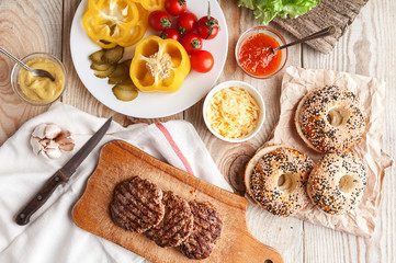 Ingredients for a delicious home burger on a wooden background. roll, bagel, with a juicy cutlet from beef, sauces cheese fresh lettuce leaves