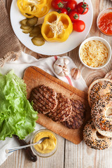 Ingredients for a delicious home burger on a wooden background. roll, bagel, with a juicy cutlet from beef, sauces cheese fresh lettuce leaves