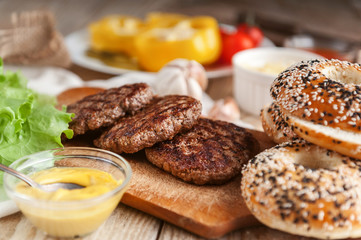 Ingredients for a delicious home burger on a wooden background. roll, bagel, with a juicy cutlet from beef, sauces cheese fresh lettuce leaves