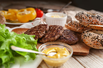 Ingredients for a delicious home burger on a wooden background. roll, bagel, with a juicy cutlet from beef, sauces cheese fresh lettuce leaves