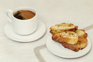 A Cup of coffee and cookies biscotti on the table in a white bowl. Selective focus. Place for text. Retro toned.