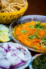 Close up of Dal makhani an Indian meal dish for lunch with sliced cucumber,onions and hari chutney with roti and white Khichdi.