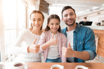 Mom, dad and little daughter are posing for a camera in a cafe.
