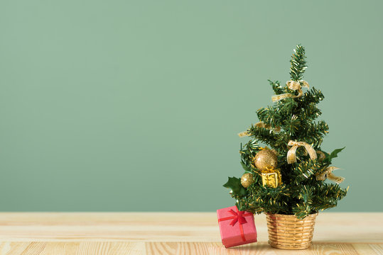 Christmas background. Little Christmas tree with decorations on a light wooden table. Green background. Space for text. New Year's background.