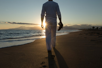 Young sexy man is walking bare foot on a beautiful sunset beach at the ocean. stand in water and...