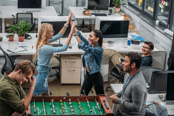 colleagues celebrating victory in table soccer at modern office