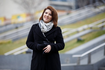 Photo of smiling brunette in black coat and scarf on blurred background