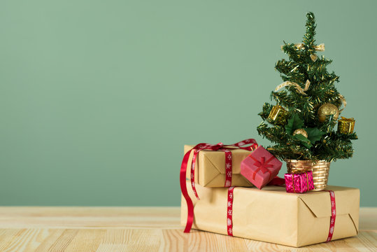 Christmas background. A small Christmas tree and boxes with gifts on a wooden table. Green background. Space for text. New Year's background.