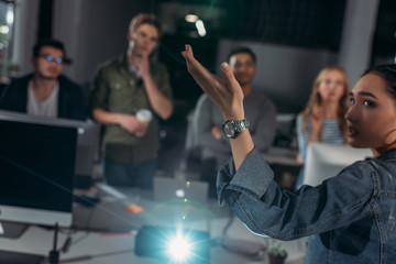 Young people watching presentation in modern office, woman pointing on screen
