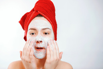 beautiful girl with a red towel on her head applies a scrub on the face of a large portrait on a...