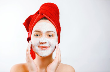 happy beautiful girl with a red towel on her head applies a scrub on the face of a large portrait on a white background