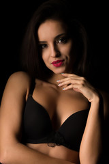 Seductive tanned woman with bright makeup and long hair posing in black bra. Shadow and light