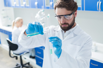 Serious professional chemist pouring liquid into the different test tube