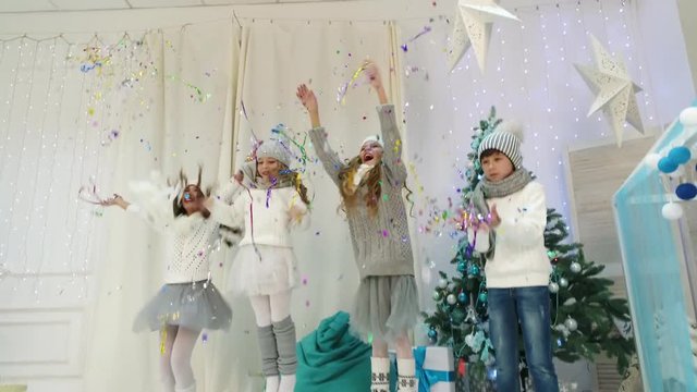Happy children in knitted sweaters and caps jumping and throwing tinsel into the air