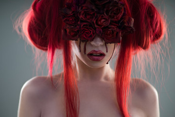 Portrait of red haired woman with flower mask and blood on face posing at camera on grey background