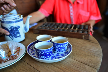 3 small cups of Chinese tea on wooden table with some snack blurry background with Chinese calculator and orange t-shirt
