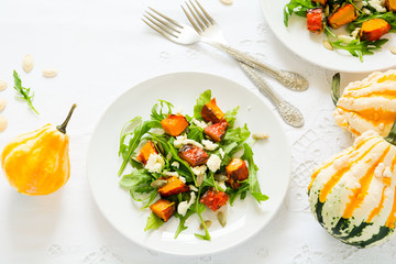 Fresh autumn salad with baked pumpkin, arugula, cheese and seeds on white table cloth. Space for copy