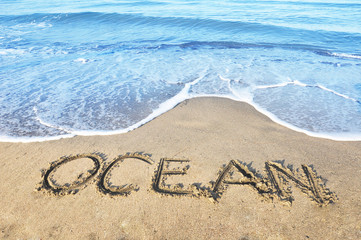 Word Ocean written on the beach with blue waves around