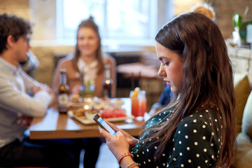 woman with smartphone and friends at restaurant