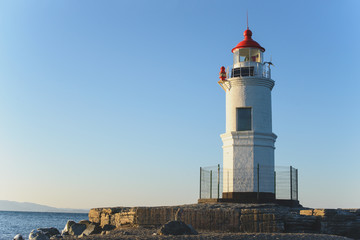 Fototapeta na wymiar Lighthouse on the seacoast at sunset light.