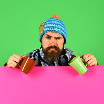 Man in warm hat holds brown and green cups