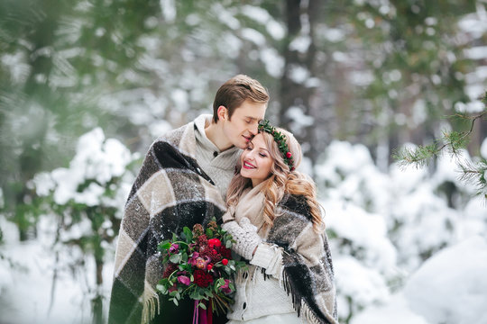 Cheerful newlyweds under the plaid are walking in winter forest. Artwork.