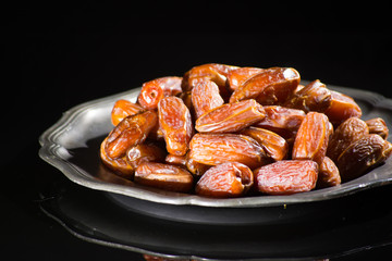 Sweet dessert dried date in old tin bowl, low key, dark theme, on black background with reflection