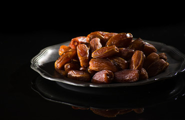 Sweet dessert dried date in old tin bowl, low key, dark theme, on black background with reflection